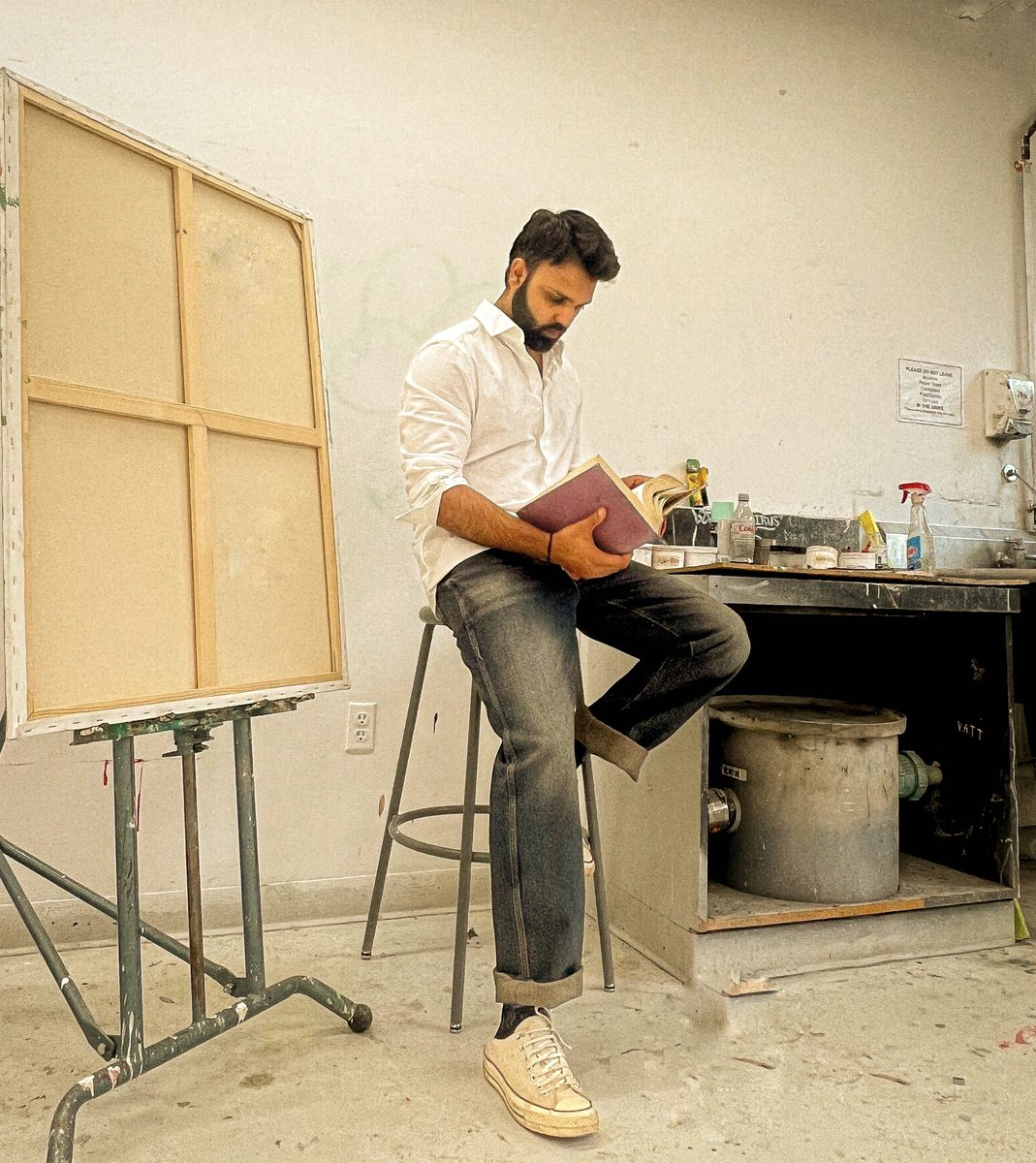 The artist in his studio, reading beside a blank canvas on an easel